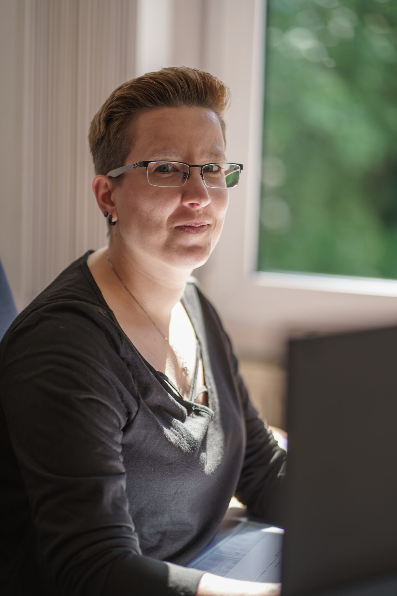 Frau die in die Kamera schaut, sitzend am Schreibtisch